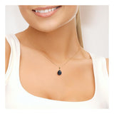 Une femme sourit, vêtue d'un haut blanc sans manches et portant le Pendentif ORÉA de Perlinea : un collier élégant ou jaune avec une perle de culture noire de Tahiti de 9-10 mm. Le fond est uni et de couleur claire.