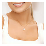 Une femme vêtue d'un haut blanc sans manches sourit, mettant en valeur son cou orné du Perlinea Pendentif ORÉA : une délicate chaîne en or ornée d'une élégante perle de culture blanche de 9-10 mm.