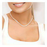 Une femme sourit, montrant ses dents, portant un haut blanc sans manches et le Perlinea Collier NOELYSE - un collier de perles blanches d'argent et de 5/6 mm avec un fermoir mousqueton - visible sur le bas du visage, le cou et le haut de la poitrine.