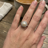 Bague en argent 925 avec perle blanche centrale entourée de zircons, portée à l'annulaire.
