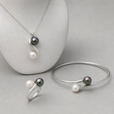 Parure toi et moi bague, bracelet et collier à perles blanches et noires sur fond gris.