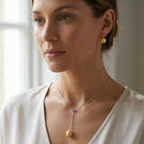 Collier et boucles d'oreilles à perles dorées portés au cou et à l'oreille.