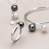 Parure toi et moi bague, bracelet et collier aux perles blanches et noires sur fond beige.